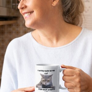 May include: White ceramic mug featuring a black and white image of a cat with the text "I work hard so my cat can have a happy life."