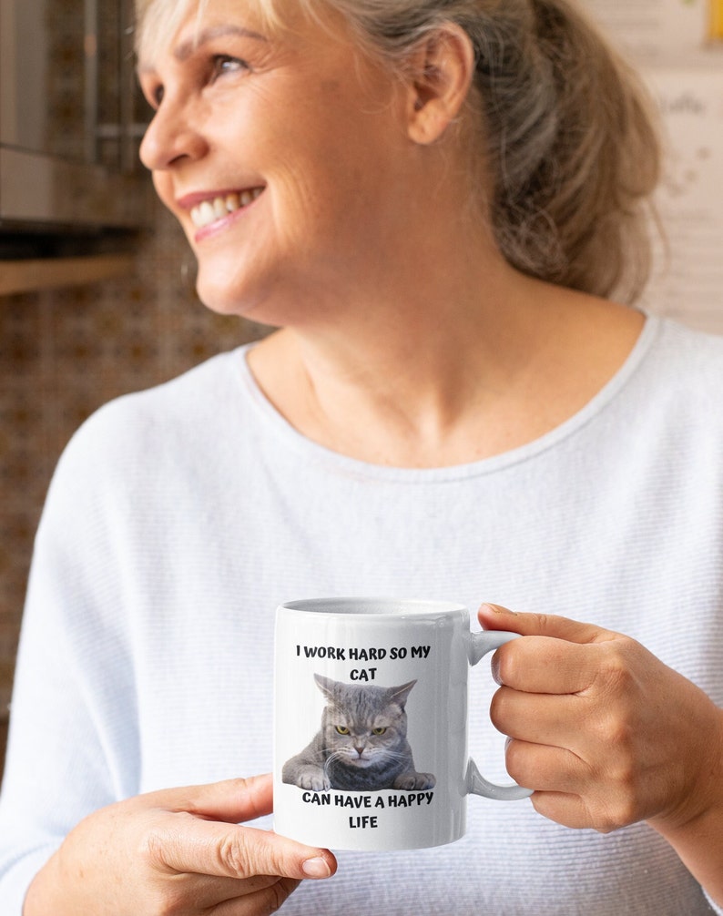May include: White ceramic mug featuring a black and white image of a cat with the text "I work hard so my cat can have a happy life."