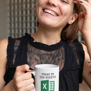 Puede incluir: Taza de cer&aacute;mica blanca con asa negra. La taza tiene un gr&aacute;fico verde y negro del logotipo de Microsoft Excel y el texto "Freak in the sheets".