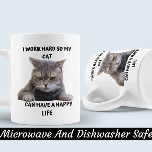 May include: White ceramic mug featuring a grey cat image and the text "I work hard so my cat can have a happy life". The mug is microwave and dishwasher safe.