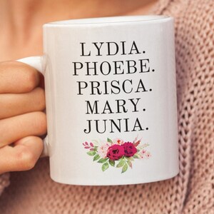 May include: White ceramic mug with black text that reads "LYDIA. PHOEBE. PRISCA. MARY. JUNIA."  The mug has a floral design with pink and white flowers.