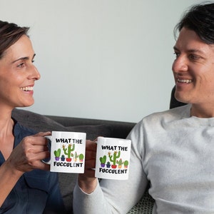 May include: Two white mugs with a cactus design and the text "What the Fuc*ulent" on them. The mugs are being held by two people.