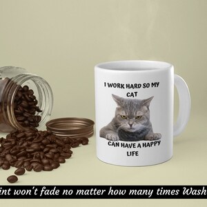 May include: White ceramic mug featuring a grey cat illustration and the text "I work hard so my cat can have a happy life".