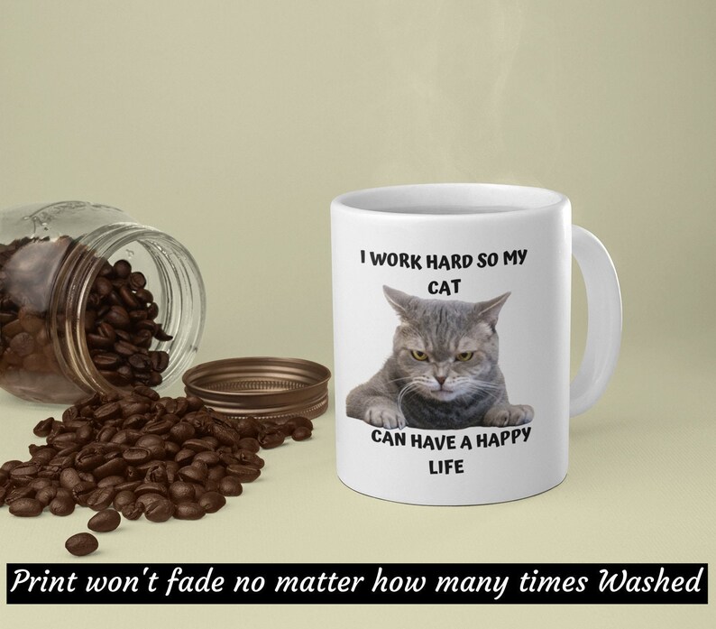 May include: White ceramic mug featuring a grey cat illustration and the text "I work hard so my cat can have a happy life".