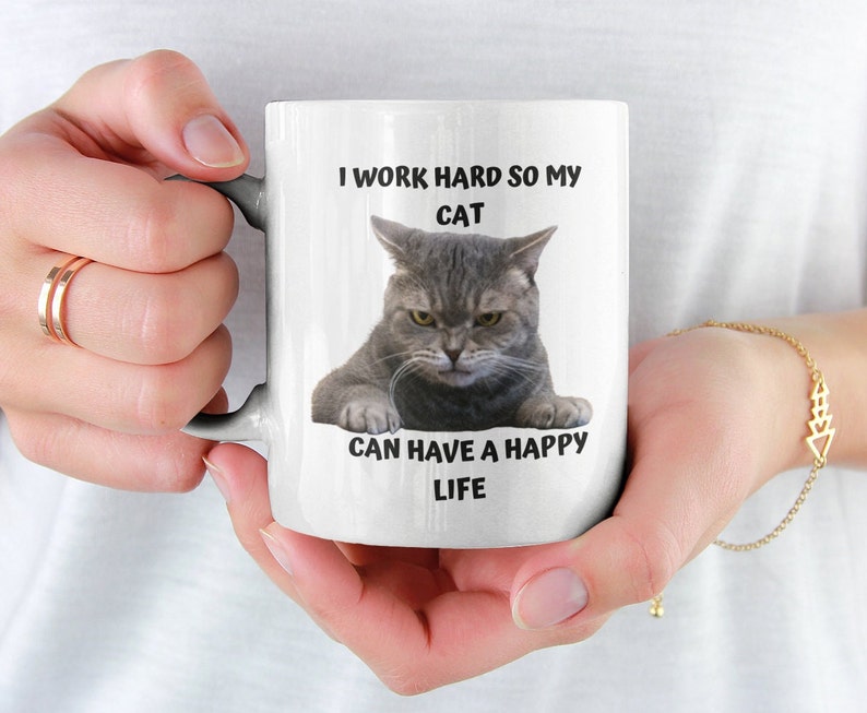 May include: White ceramic mug featuring a black and white image of a cat with the text "I work hard so my cat can have a happy life."