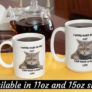 May include: Two white ceramic mugs with black text and a picture of a cat. The text on the mugs reads "I work hard so my cat can have a happy life". The mugs are available in 11oz and 15oz sizes.