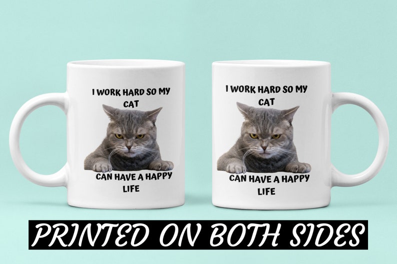 May include: White ceramic coffee mug featuring a grey cat image and the text "I work hard so my cat can have a happy life". The text is printed on both sides of the mug.