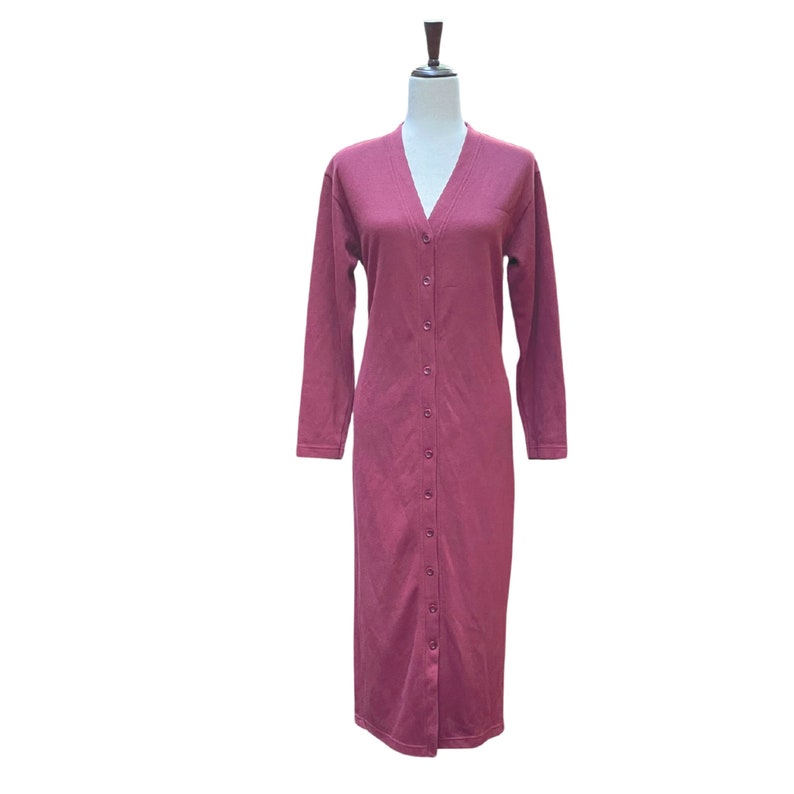 May include: A long, button-down dress in a deep burgundy color. The dress features a V-neckline and long sleeves. The dress is displayed on a mannequin against a white background.