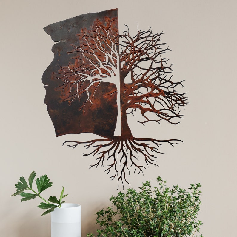 May include: Metal wall art sculpture of a tree with roots and branches. The tree is made of two pieces of metal, one with a rusty brown finish and the other with a white finish. The tree is mounted on a white wall.