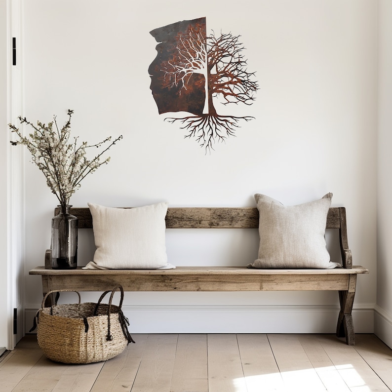 May include: A rustic wooden bench with two pillows sits in front of a white wall with a metal tree wall art sculpture. The tree is made of metal and has a brown and white finish. The sculpture is mounted on the wall.