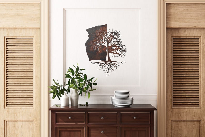 May include: A metal wall art sculpture of a tree with roots and branches, half of the tree is a rusty brown color and the other half is white. The sculpture is hanging on a white wall above a wooden dresser with two drawers.