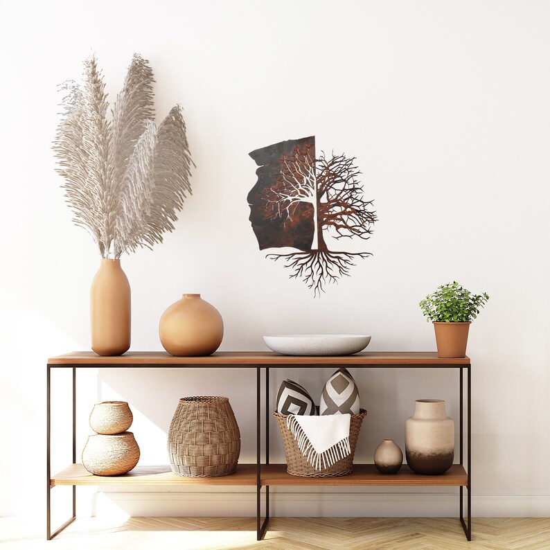 May include: A metal wall sculpture of a tree with roots, with a rusty brown finish and white branches. The sculpture is hanging on a white wall above a wooden console table with two shelves. The table is decorated with a vase, a bowl, baskets, and other decorative items.