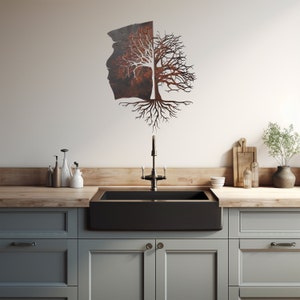 May include: A rustic metal tree wall art with a split trunk and intricate roots. The tree is mounted on a white wall above a black farmhouse sink in a kitchen.