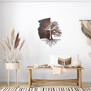 May include: A rustic metal wall art piece depicting a tree with roots and branches. The tree is split in half, with one side showing a brown, textured surface and the other side showing a bare tree with white branches. The art piece is hanging on a white wall with a beige rug, a wooden bench, and two vases with dried plants.