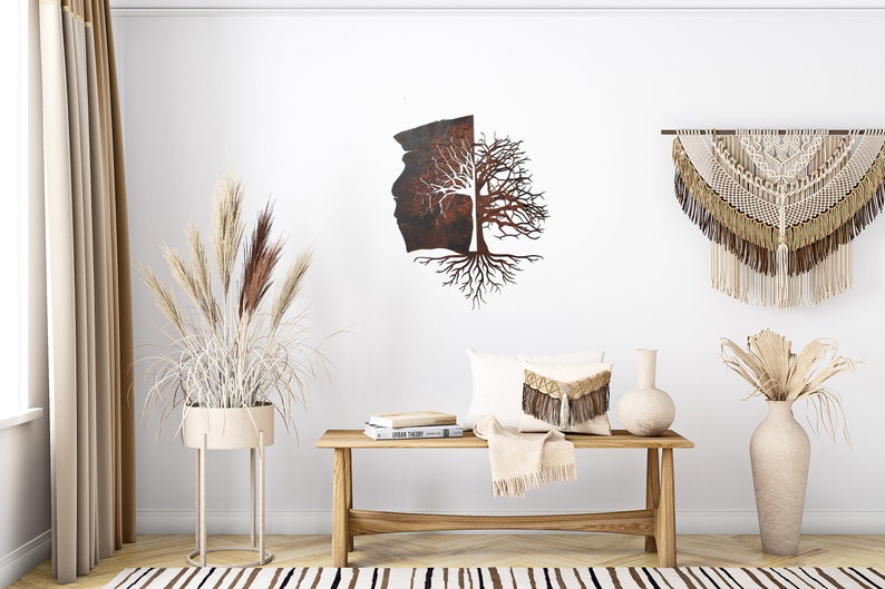 May include: A rustic metal wall art piece depicting a tree with roots and branches. The tree is split in half, with one side showing a brown, textured surface and the other side showing a bare tree with white branches. The art piece is hanging on a white wall with a beige rug, a wooden bench, and two vases with dried plants.