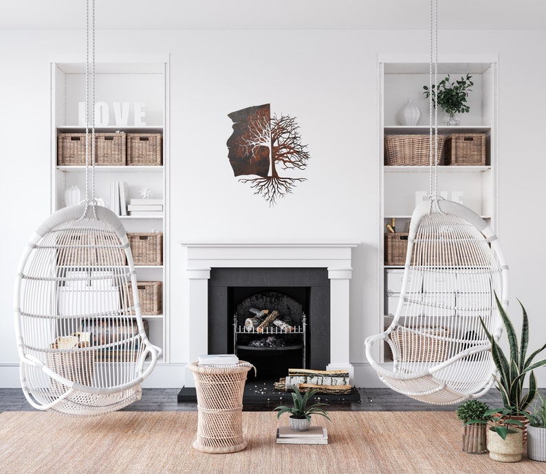 May include: A white wicker hanging chair with a metal tree sculpture on the wall behind it. The tree sculpture is made of metal and has a brown and black finish. The chair is hanging from the ceiling and is in a living room setting.