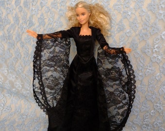 May include: A black lace doll dress with long sleeves and a high neckline. The dress is worn by a doll with blonde hair and blue eyes.