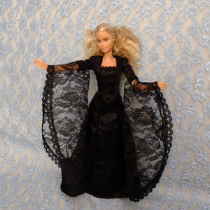 May include: A black lace doll's dress with long sleeves and a high neckline. The dress is being worn by a doll with blonde hair and blue eyes.