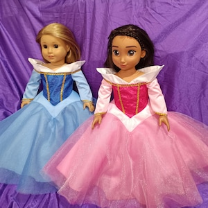 Puede incluir: Dos muñecas vestidas con vestidos de princesa. Una muñeca lleva un vestido azul claro con un corpiño azul y ribetes dorados. La otra muñeca lleva un vestido rosa con un corpiño rosa y ribetes dorados. Ambas muñecas tienen faldas largas y fluidas.