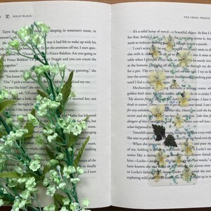 Könnte beinhalten: Nahaufnahme eines geöffneten Buches mit gepressten Blumen und Blättern auf den Seiten. Der Text auf der Seite lautet: "Es ist ein massiver Klumpen aus Metall - ein wunderschönes Objekt. Zuerst nehme ich es nur dafür, bevor ich bemerke..."