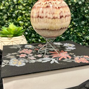 May include: A large, white and red striped sphere made of polished stone, sitting on a metal stand. The sphere is on a black surface with a floral pattern.