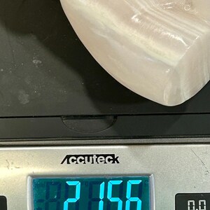 May include: A white, smooth, and slightly translucent stone sculpture is being weighed on a digital scale. The scale reads 2.156 lb. The scale is silver and has a black display. The scale is labeled "Accuteck" and has a maximum weight capacity of 50 lb. The scale also has a precision of 0.1 oz.