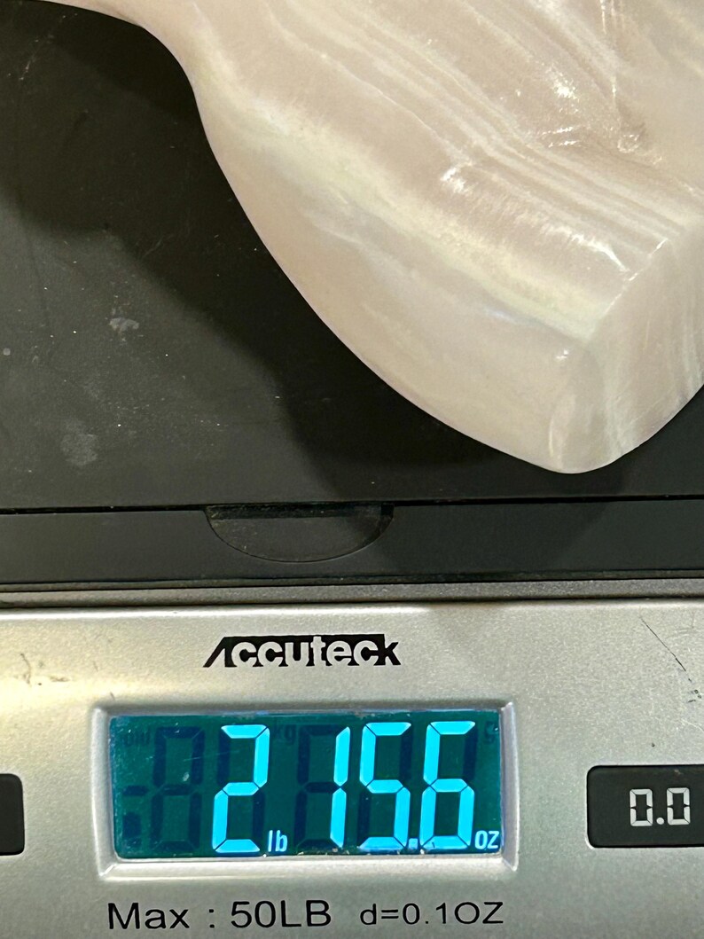 May include: A white, smooth, and slightly translucent stone sculpture is being weighed on a digital scale. The scale reads 2.156 lb. The scale is silver and has a black display. The scale is labeled "Accuteck" and has a maximum weight capacity of 50 lb. The scale also has a precision of 0.1 oz.
