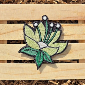 May include: A green and white embroidered flower patch with a black outline. The flower has five petals and a white center. The patch is perfect for adding a touch of nature to your clothing or accessories.