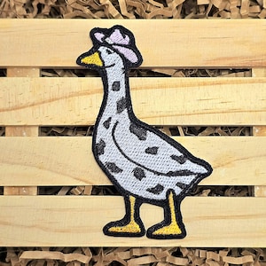 May include: A gray goose with black spots wearing a pink hat. The goose is standing on a wooden surface.