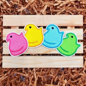 May include: Four embroidered iron-on patches shaped like marshmallow peeps. The patches are pink, yellow, blue, and green.