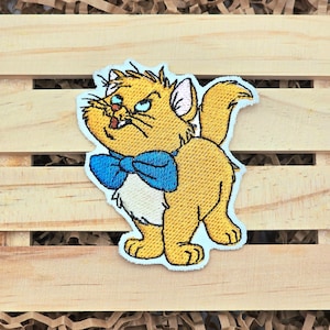 May include: An embroidered iron-on patch of a cartoon cat with a blue bow tie. The cat is yellow with white fur and has a mischievous expression.