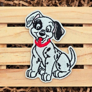 May include: Embroidered patch of a cartoon Dalmatian puppy sitting with its tongue sticking out, wearing a red collar. The patch is white with black spots and has a white outline.