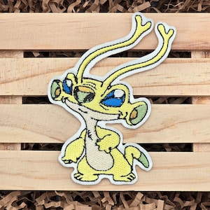 May include: Yellow embroidered patch of a cartoon alien with large eyes and antennas. The alien is standing with its arms crossed and has a friendly expression.