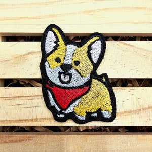 May include: Embroidered patch of a cartoon dog with yellow and white fur, wearing a red bandana. The dog is looking to the right.