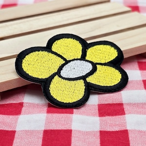 May include: A yellow embroidered flower patch with a white center and black outline. The patch is on a red and white checkered background.