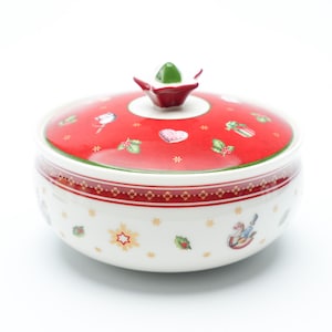 Könnte beinhalten: Eine weiße und rote Keramik-Servierschüssel mit Deckel. Der Deckel ist rot mit weihnachtlichen Illustrationen. Die Schüssel hat einen weißen Boden mit festlichen Designs. Ein grüner und roter Blumenstiel ziert den Deckel.