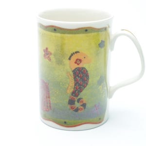 Peut inclure: Tasse en céramique blanche avec un motif d'hippocampe et d'étoiles de mer. La tasse présente un hippocampe avec un motif rouge et noir, entouré de créatures marines sur un fond vert et jaune. La tasse a une anse et un bord blancs.
