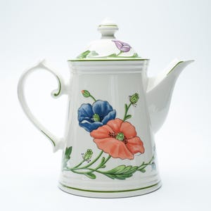 May include: White ceramic teapot with a lid, handle, and spout. The teapot is decorated with a floral design featuring blue and coral-colored poppies, green leaves, and buds. The rim and handle have green accents.
