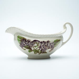 Peut inclure: Saucière en céramique blanche ornée d'un motif floral de fleurs violettes et de feuilles vertes. Elle est dotée d'une anse incurvée et d'un bord festonné. Un classique pour les sauces.
