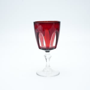 Op de afbeelding: Een rood wijnglas met een heldere steel en voet. Het glas heeft een gesneden ontwerp op de kom.
