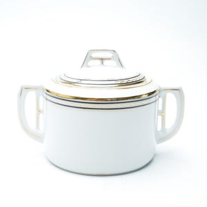 May include: White porcelain sugar bowl with a lid, featuring gold and navy blue trim. The bowl has two handles and a matching lid with a decorative top. A classic piece for serving sugar or other condiments.