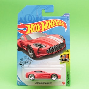 Könnte beinhalten: Ein rotes Hot Wheels-Spielzeugauto aus Metallguss, der Aston Martin One-77, in einer blauen und gelben Pappverpackung. Das Auto hat weiße Rennstreifen und ist Teil der HW Exotics-Serie.