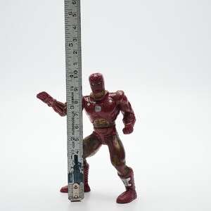 Pode incluir: Figura de a&ccedil;&atilde;o de pl&aacute;stico vermelho e dourado do Homem de Ferro em pose de luta. A figura mede aproximadamente 15 cm de altura.