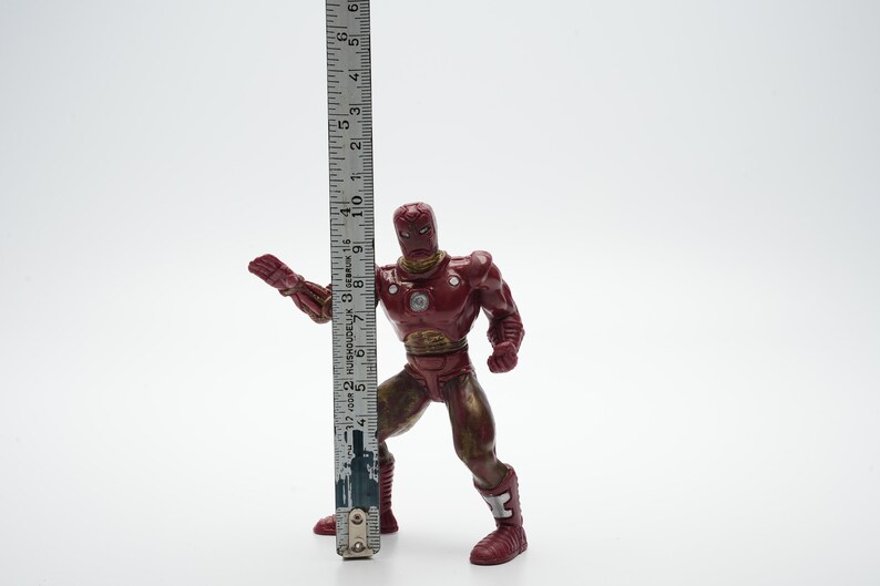 Pode incluir: Figura de a&ccedil;&atilde;o de pl&aacute;stico vermelho e dourado do Homem de Ferro em pose de luta. A figura mede aproximadamente 15 cm de altura.