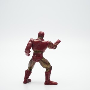 Pode incluir: Uma figura de a&ccedil;&atilde;o de um super-her&oacute;i vermelho e dourado em p&eacute; com um bra&ccedil;o levantado. A figura &eacute; feita de pl&aacute;stico e tem um design detalhado.