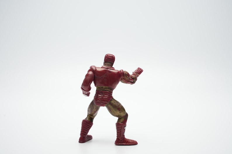 Pode incluir: Uma figura de a&ccedil;&atilde;o de um super-her&oacute;i vermelho e dourado em p&eacute; com um bra&ccedil;o levantado. A figura &eacute; feita de pl&aacute;stico e tem um design detalhado.