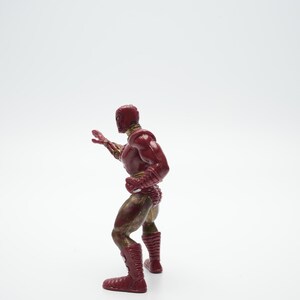 Pode incluir: Uma figura de a&ccedil;&atilde;o vermelha e dourada de um super-her&oacute;i em p&eacute; com um bra&ccedil;o levantado. A figura est&aacute; em posi&ccedil;&atilde;o de luta.