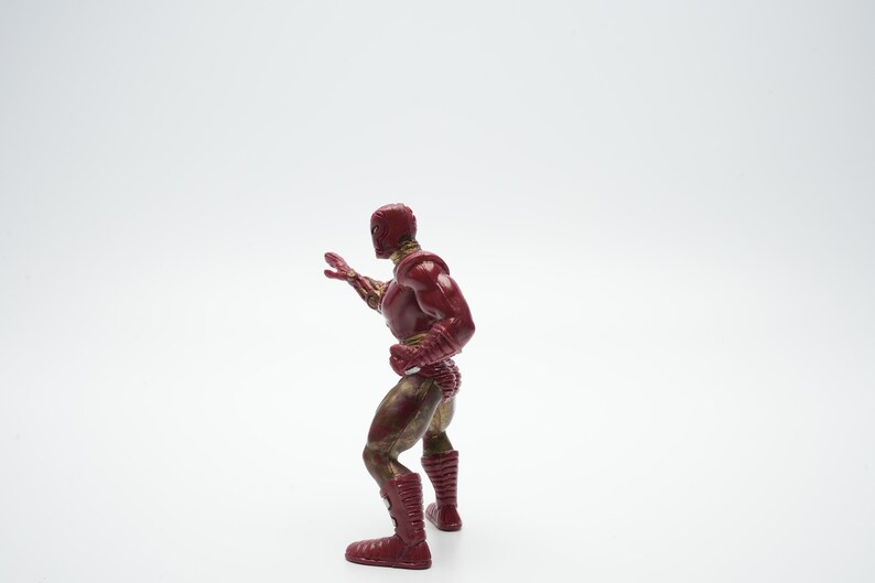 Pode incluir: Uma figura de a&ccedil;&atilde;o vermelha e dourada de um super-her&oacute;i em p&eacute; com um bra&ccedil;o levantado. A figura est&aacute; em posi&ccedil;&atilde;o de luta.