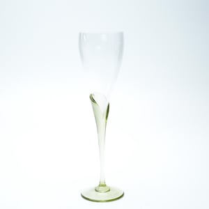 May include: A tall, elegant champagne flute with a unique, curved design. The glass has a slender stem and a wide, rounded base. The glass is clear with a subtle green tint, and the design adds a touch of sophistication to any occasion.