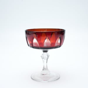 May include: A clear glass stemmed goblet with a red, faceted bowl. The goblet is designed for serving champagne or other sparkling beverages.